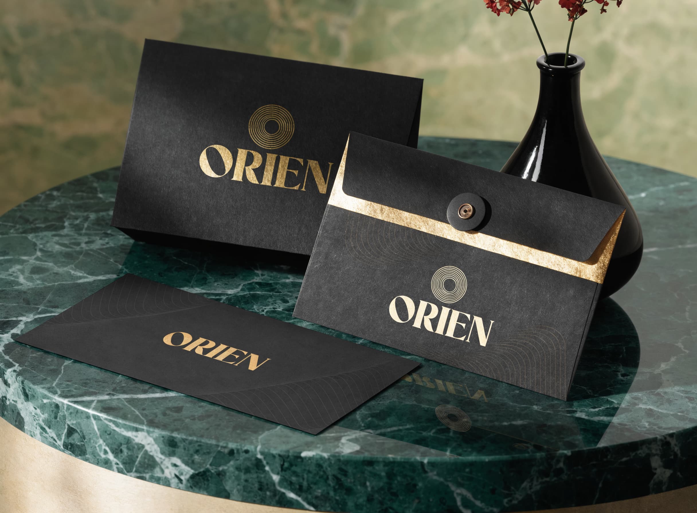 Black and gold stationery for a brand named Orien, beside a dark vase on marble